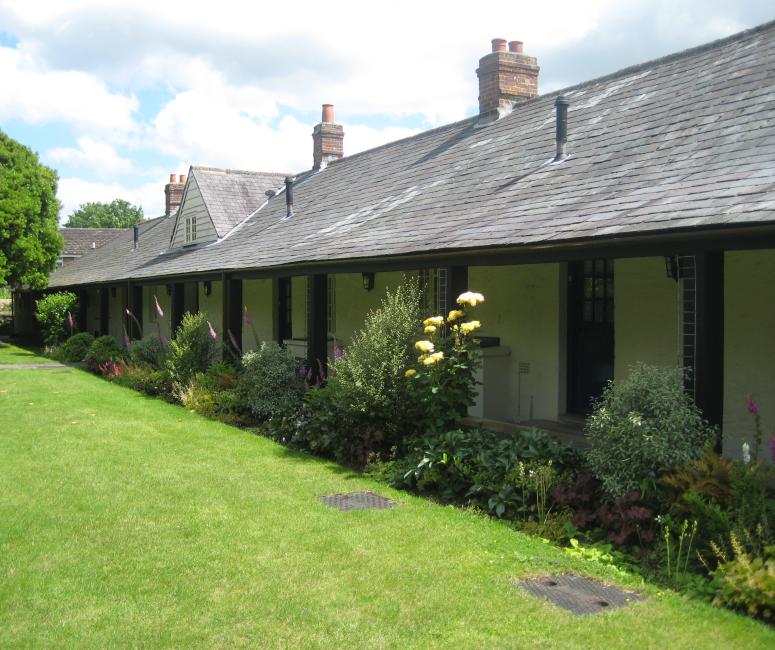 A single story brick building painted white with a grey roof and a flourishing garden.