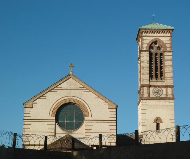 A white and red brick church building with a central circular window and a tower with a green roof to its right.