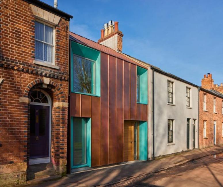 A terraced row of brick Victorian houses, with a modern building in the centre, with green copper-framed windows and rust-coloured metal cladding. 