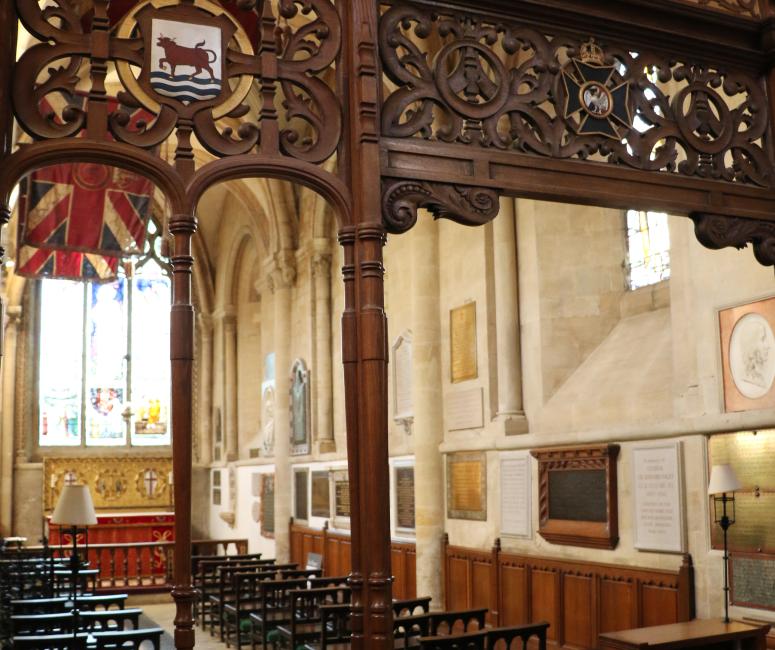 A carved wooden screen with a crest showing a red ox crossing a blue river. The screen is in front of a small stone chapel with wooden seating.