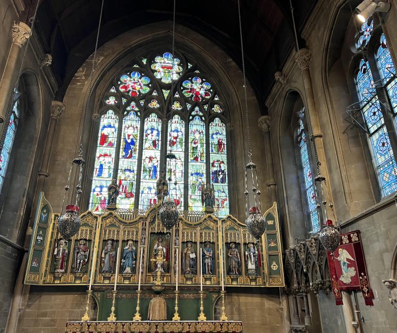 The interior of a church facing a gilt altar with a large stained glass window in the background.