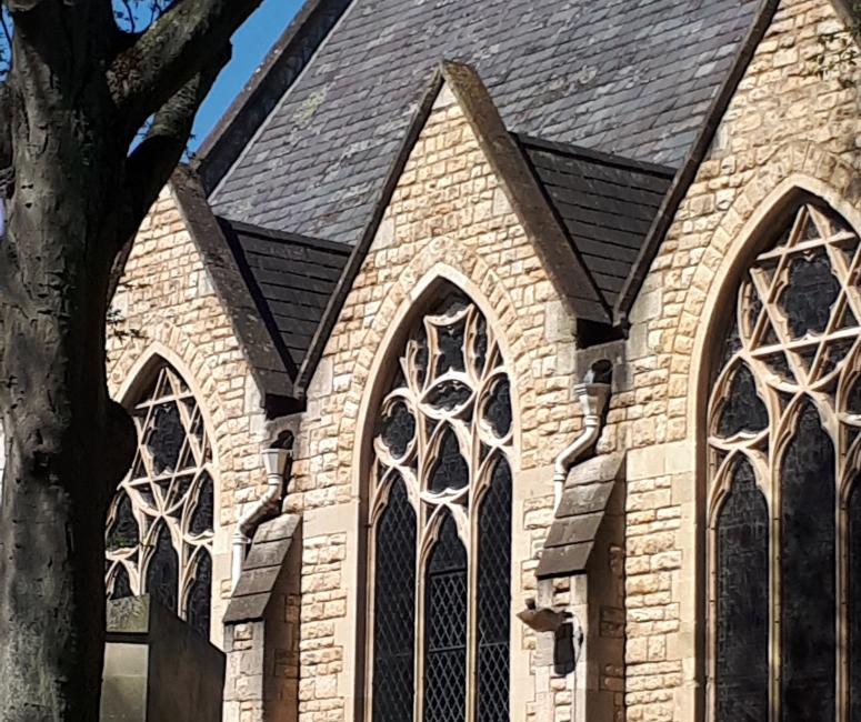 The side view of a stone church with grey roof tiles and tall arched windows.