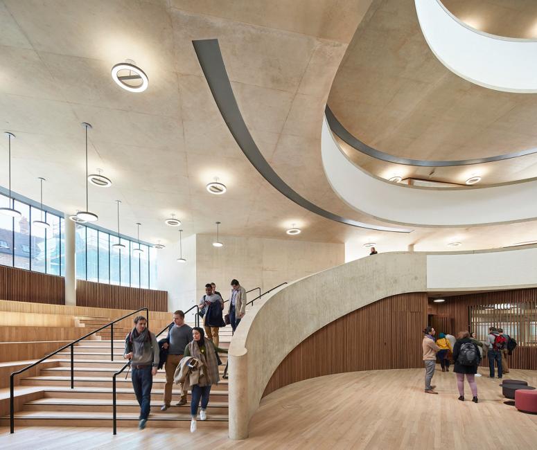 The interior of a modern curved concrete building with a curved staircase and wooden floor.