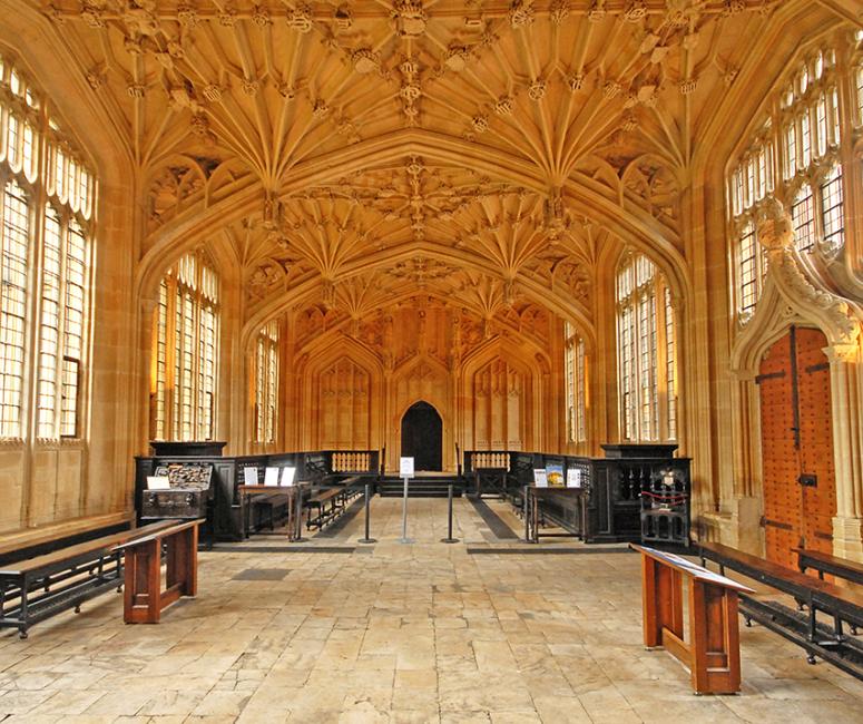 A room with an elaborate fan vaulted ceiling and wooden benches on either side.