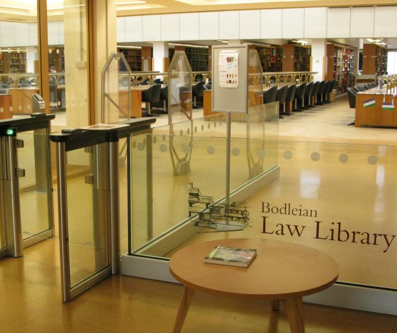 The interior of a modern library with a glass entrance scanner and rows of light wooden desks in the background. A sign reads Bodleian Law Library.