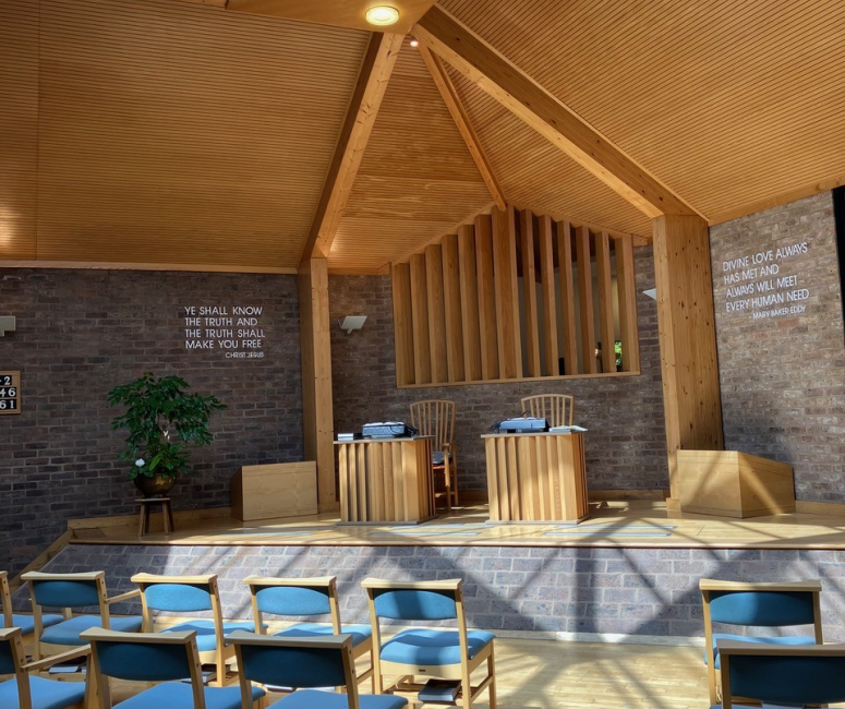 A modern church building with blue chairs laid out towards a stage with a wooden canopy.