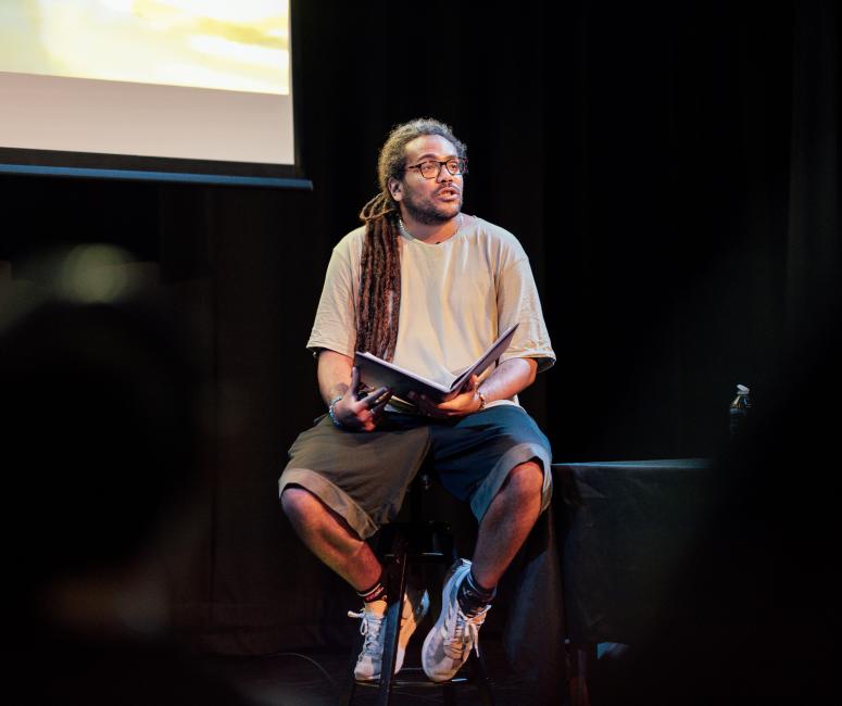 A man sits on a stool to perform poetry.