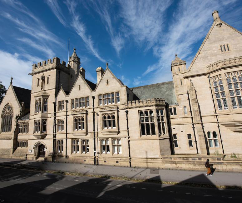 The street frontage of a large stone building with a gatehouse, several bay windows and a varied roof line.