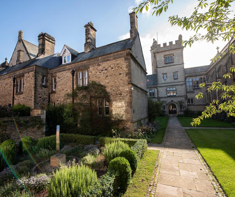 A long path through a formal garden leading to a stone building with gatetower.