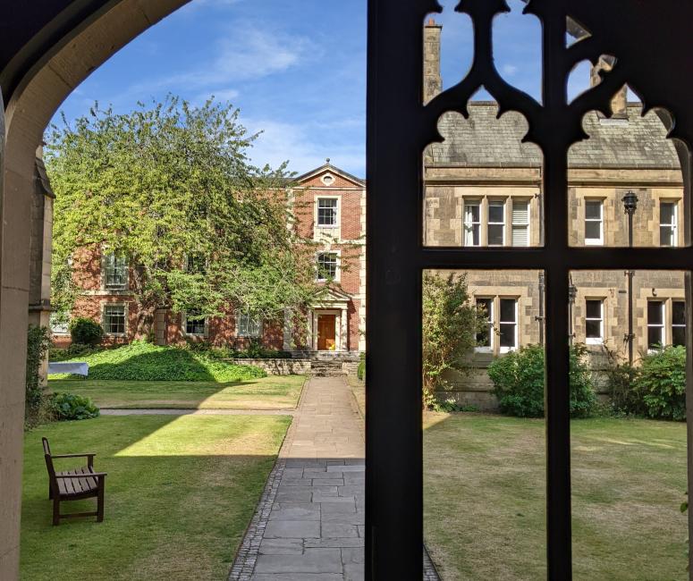 A doorway with one closed door with tracery windows and one open door looking out onto a path through a lawned garden.