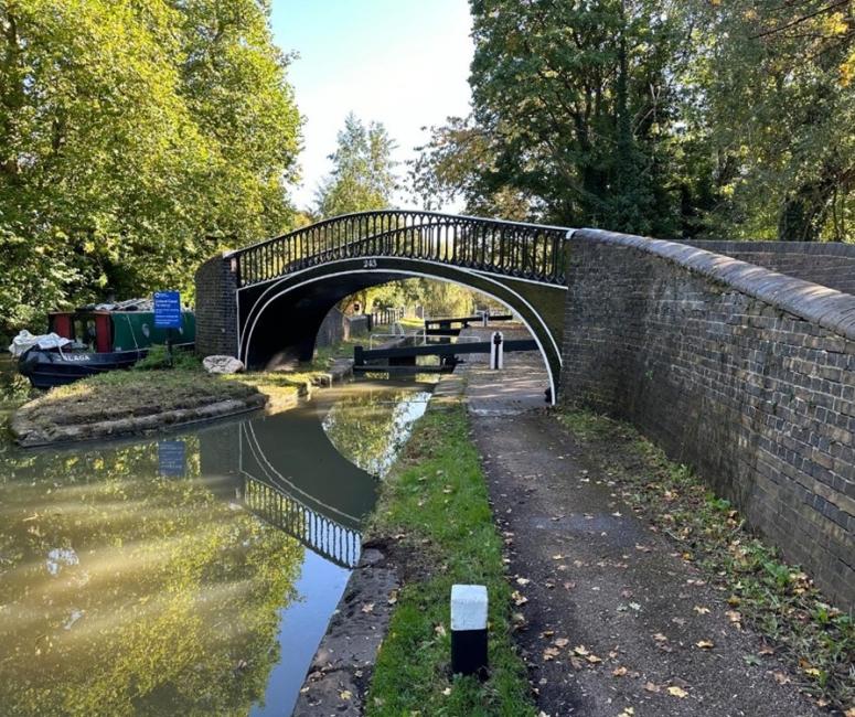 A bridge over a canal with towpaths and trees on either side.