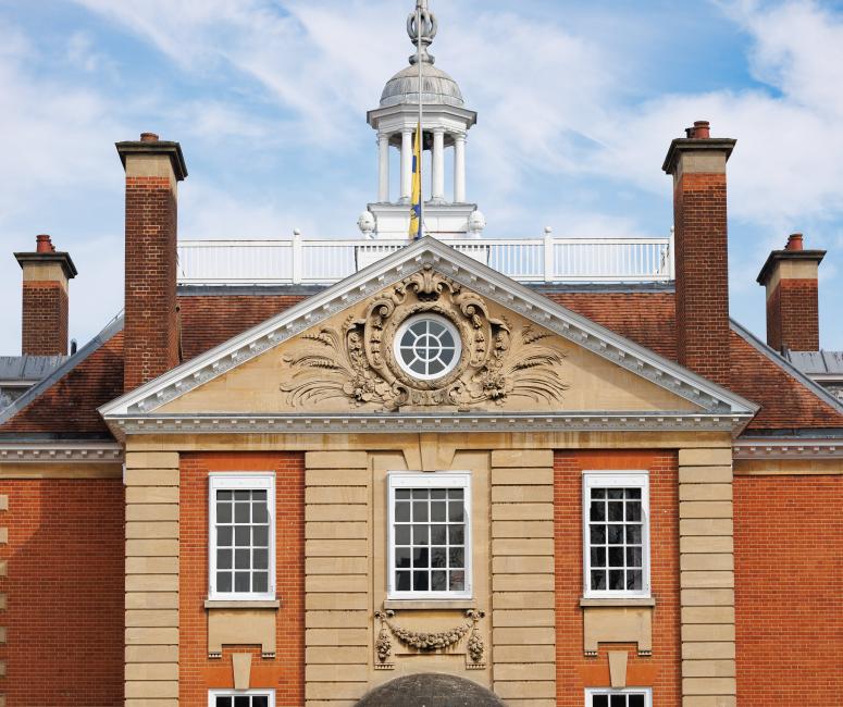 The central part of an orange brick building with pediment containing a circular window, an open cupola, and a domed ground floor doorway.