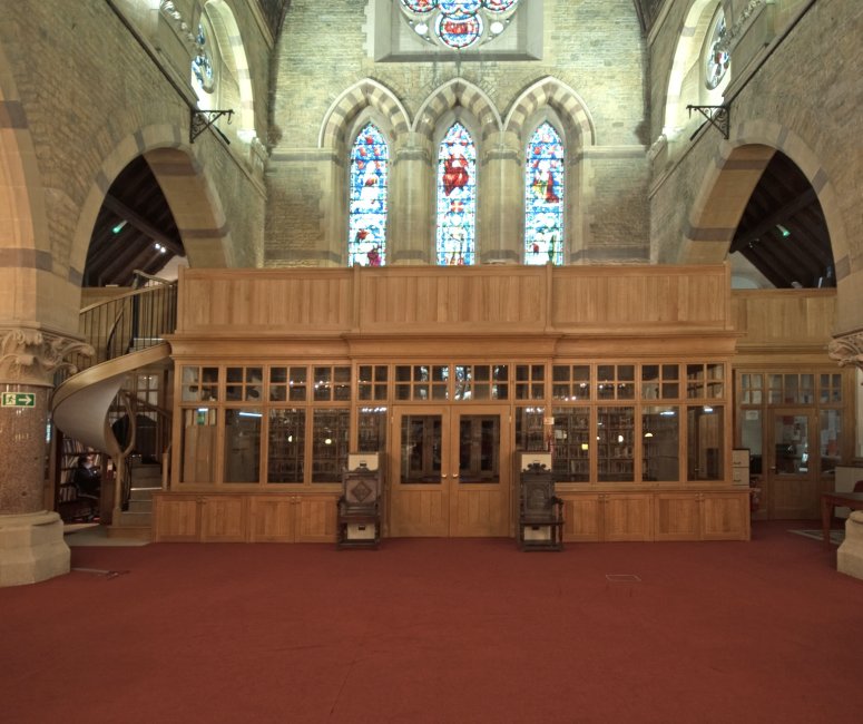 The interior of a stone church building that has been converted into a study centre with bookshelves and a wooden entrance porch.