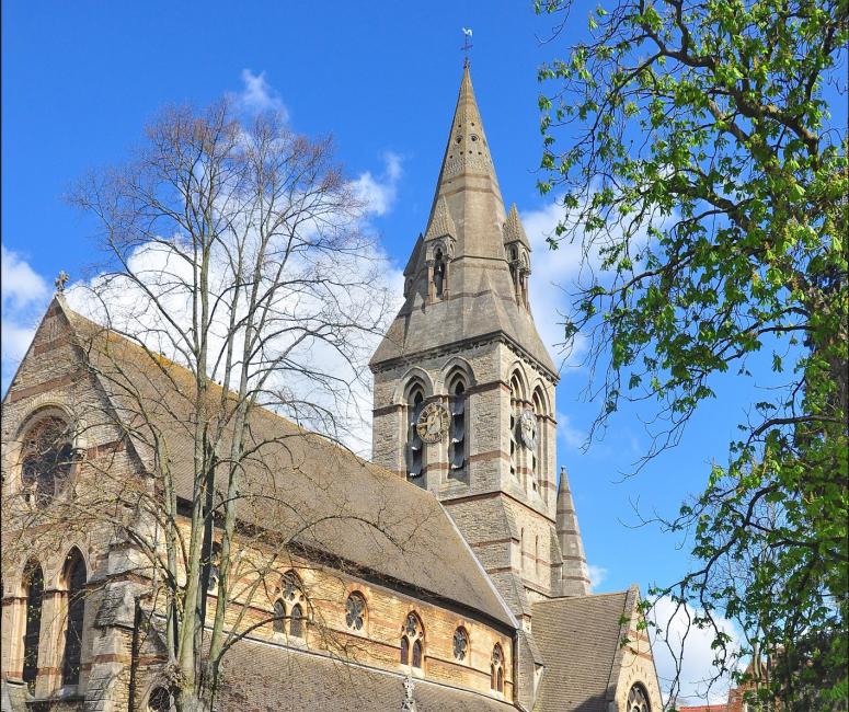A sandy-coloured church with tower and steeple in a walled churchyard.