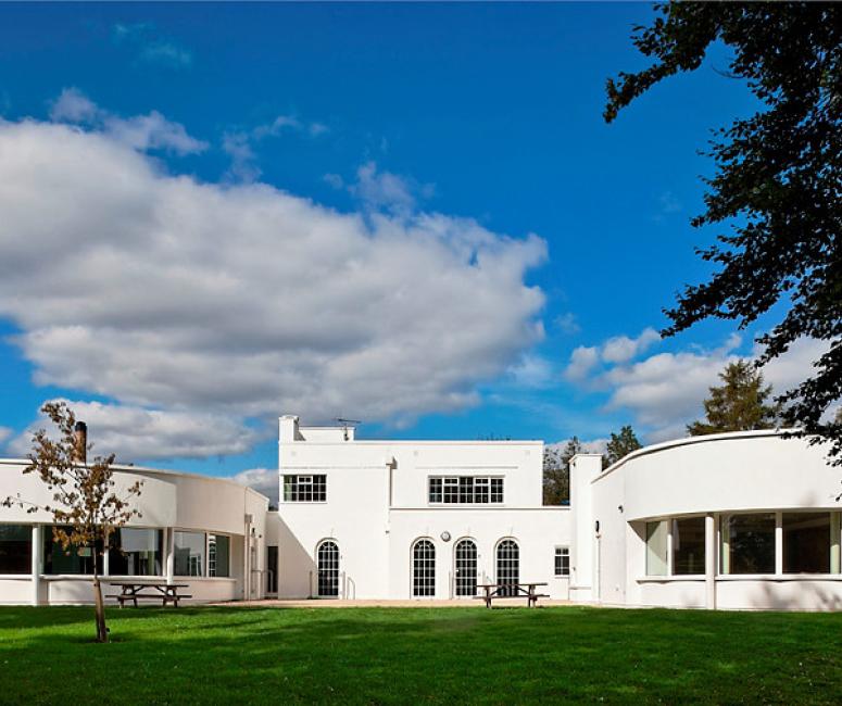 A white 1930s building with green lawns in front and blue skies behind.