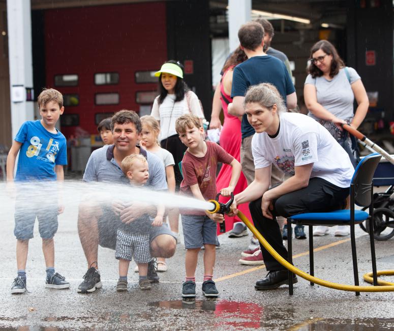 A family have a go at directing a water hose in front of a fire station.