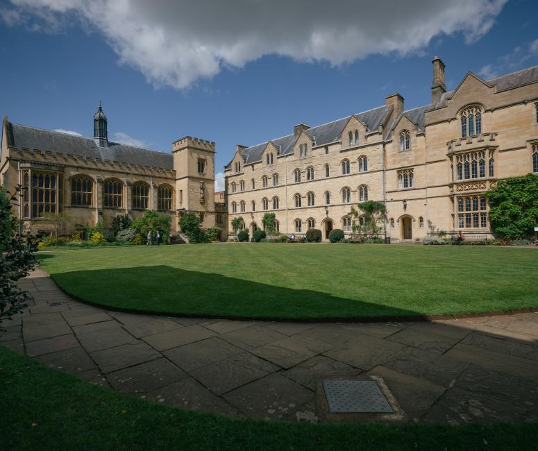 A grassy quadrangle between a large stone college building and a chapel.