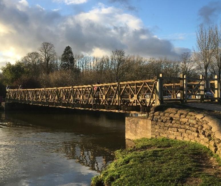 A Bailey Bridge over a river in the late afternoon sun.