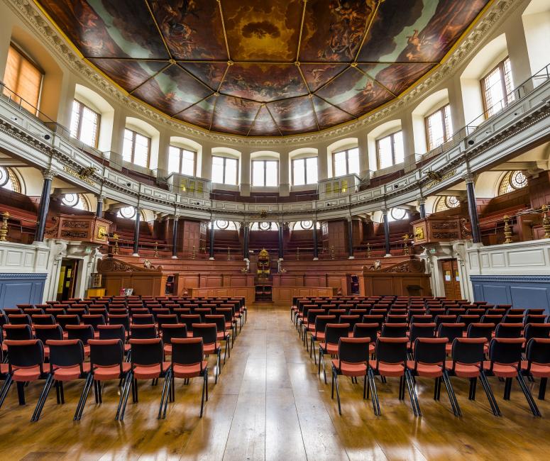 A semicircular theatre building with a painted ceiling and rows of benches and chairs.