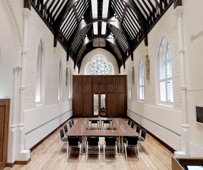 A chapel interior with bright white walls and dark wooden roof beams, with a conference style table in the centre.