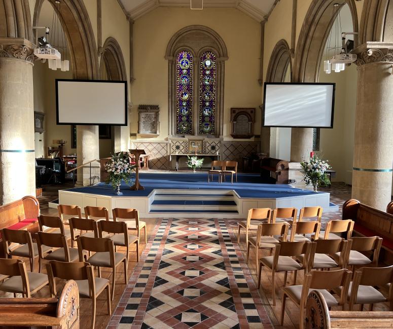 The interior of a church with rounded arched windows and rows of chairs.