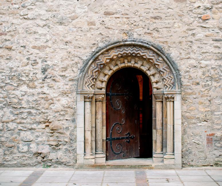 A Norman rounded doorway into a stone church with arched windows above.