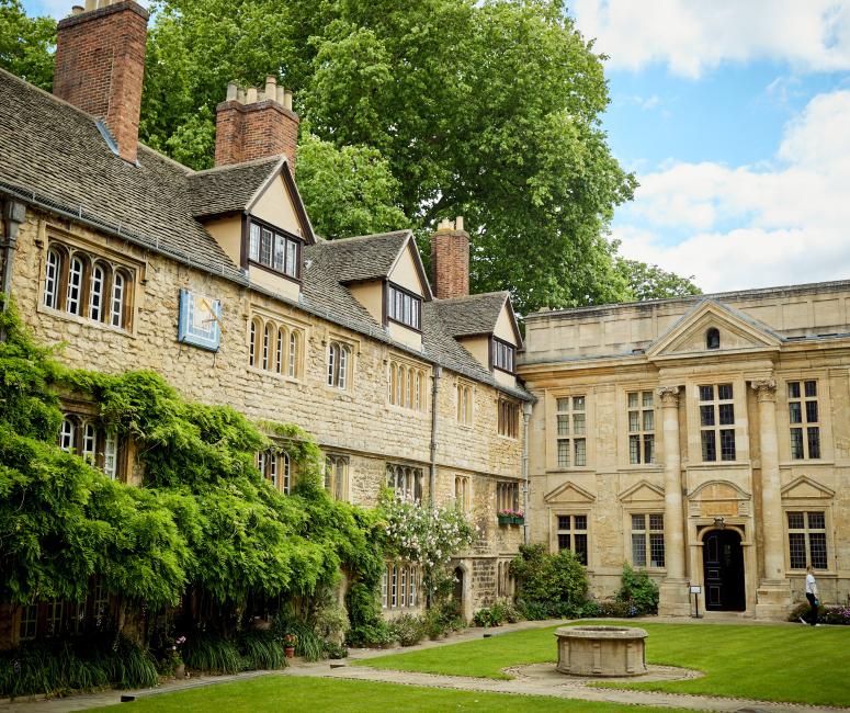 A sand-coloured stone building with gables and climbing foliage set around a grassy courtyard.