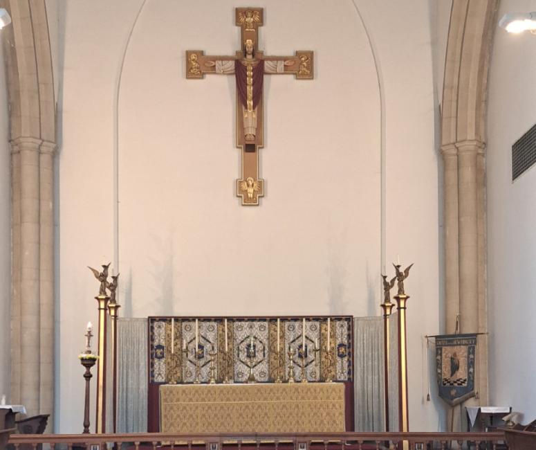 A church interior with a red carpeted altar area and a large crucifix suspended above.