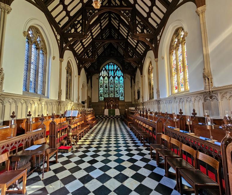 A chapel with wooden roof beams, whitewashed walls and black and white chequered tiles.
