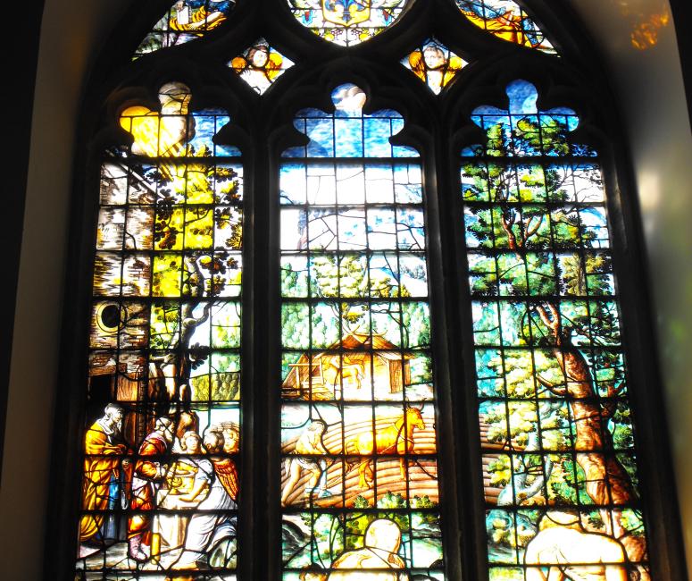 A brightly-coloured stained-glass window with figures in a landscape.