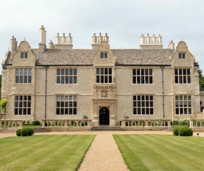 The facade of a seventeenth-century stone built manor house with large symmetrical windows, three dormers and an ornate carved entrance way.