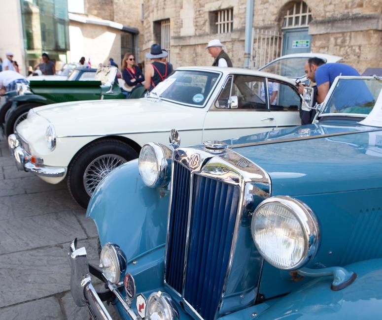 A row of blue, cream and green classic cars parked in from of Oxford Castle and Prison.