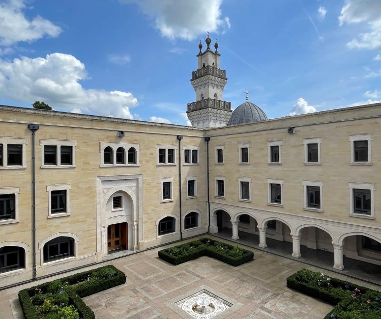 A cream-coloured buildings around a courtyard, with a minaret in the background.