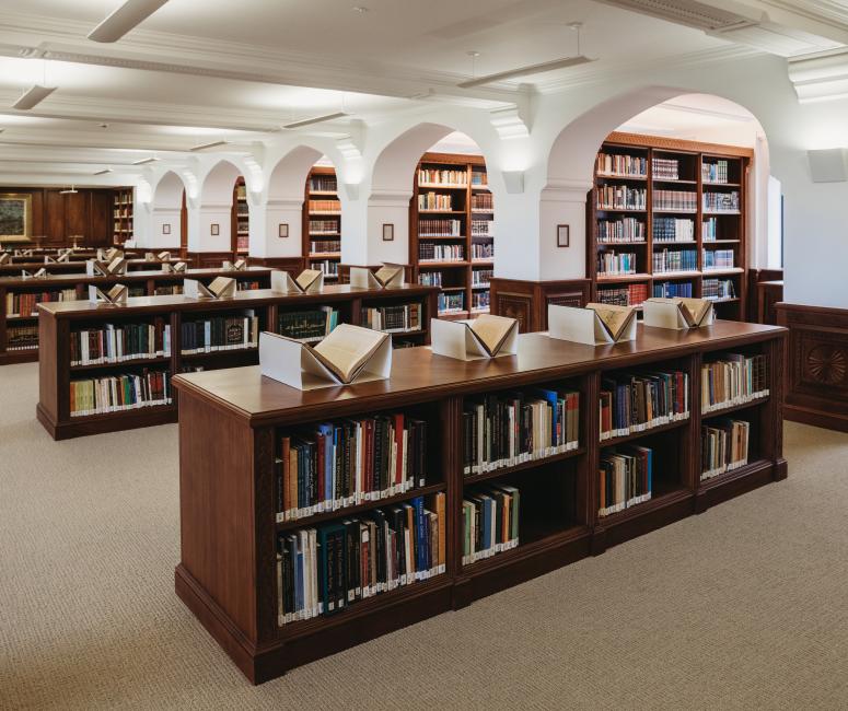 A library with brown wooden bookcases beneath white arches.