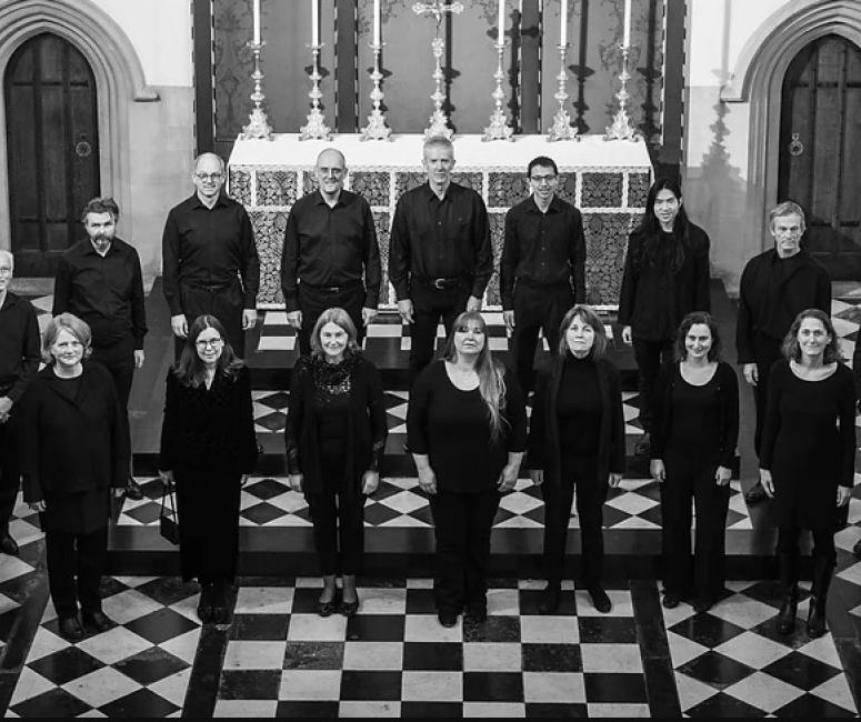 A black and white photograph of a 21-person chamber choir standing in a church with a black and white tiled floor.