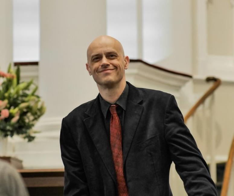 A man stands in front of a staircase wearing a jacket and tie.