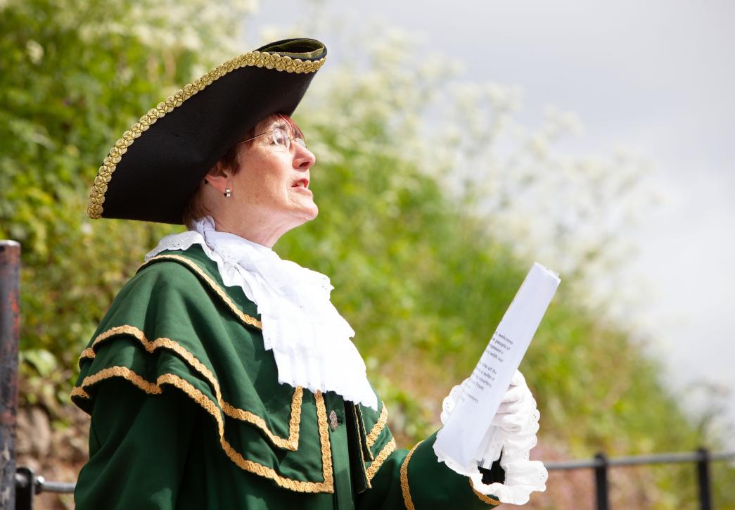 Town crier reading in front of greenery