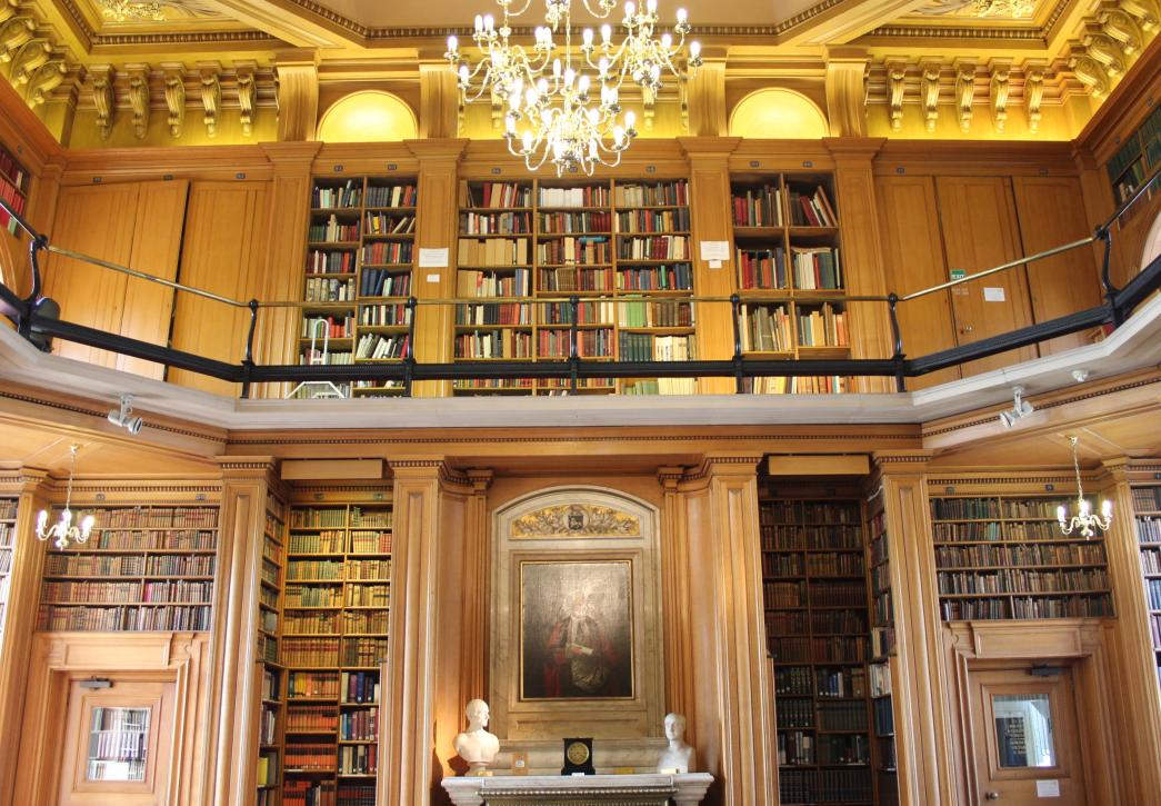 Photo of a wood-panelled library with a balcony, lit by a chandelier. 
